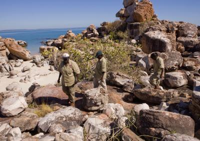 Three Indigenous rangers walking across rocks near the ocean