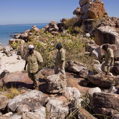Three Indigenous rangers walking across rocks near the ocean